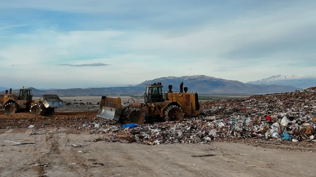 Two landfill compactors working the active face at Bayview Landfill, spreading and compacting incoming waste, with the Utah valley floor behind.