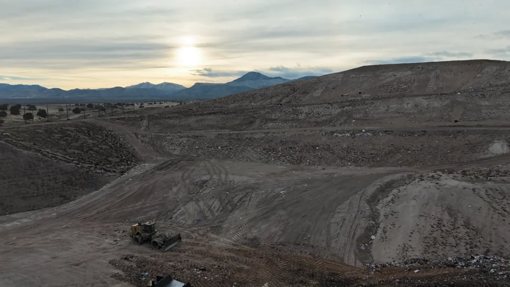 Aerial view of Bayview Landfill showing the benched, terraced disposal cells and graded haul roads, with a compactor working the lower bench at sunset.